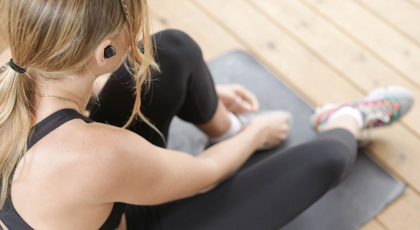 Get your workout on woman in workout gear, sits on a yoga mat and ties her shoe